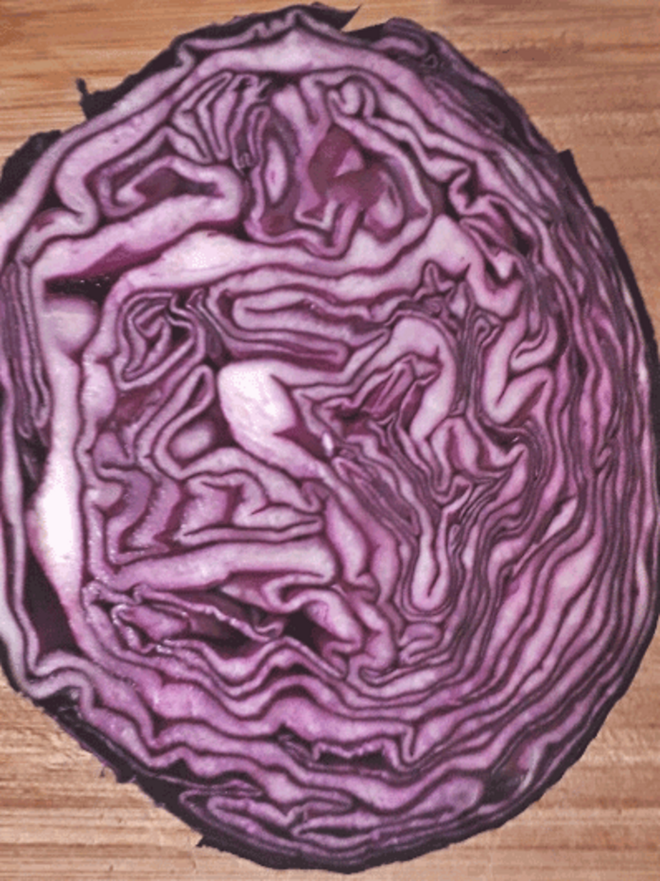 Das Bild zeigt einen Querschnitt von Rotkohl, der auf einem Holzuntergrund liegt. Die verschiedenen lila und weißen Schichten des Kohls sind deutlich sichtbar und präsentieren die charakteristische Struktur des Gemüses.