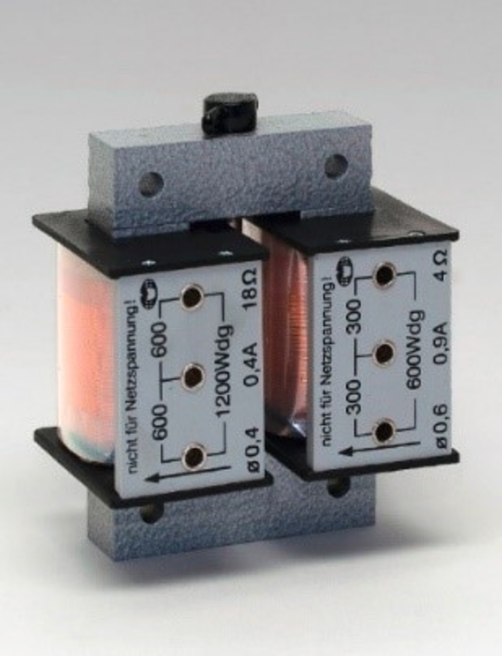 Das Bild zeigt eine elektrische Spule mit zwei Wicklungen, die auf einer stabilen Basis montiert ist. Die Spule verfügt über mehrere Anschlüsse, die für Experimente im Bereich der Elektrotechnik und Physik genutzt werden können.