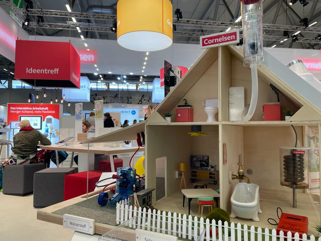 Das Bild zeigt ein Modell eines Energiewandelhauses, das mit verschiedenen Modulen rund um das Thema Solarenergie ausgestattet ist. Das Haus verfügt über eine Möblierung sowie über Installationen, einschließlich eines Wasserstoffgenerators im Außenbereich