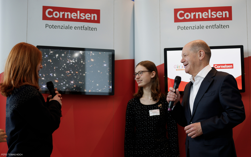 Olaf Scholz steht lächelnd mit einem Mikrofon in der Hand neben zwei Schülerinnen bei der Auftaktveranstaltung zum Girls' Day 2024 im Bundeskanzleramt.