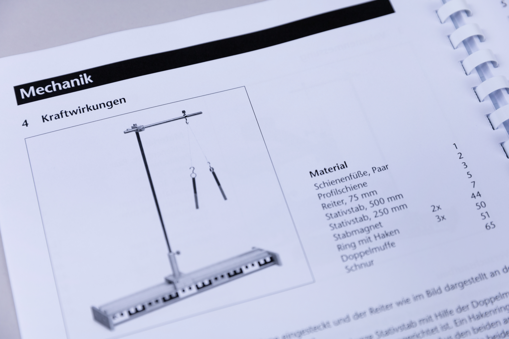 Das Bild zeigt eine Anleitung aus einem Experimentierhandbuch zur Mechanik, die ein Aufbau zur Demonstration von Kraftwirkungen illustriert. Es listet das benötigte Material auf, einschließlich Schienenfüßen, Stäben und weiteren Komponenten für das Experi