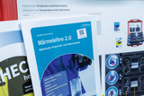 Das Bild zeigt eine Anleitung für das Experimentiergerät "Wärmelehre 2.0", das sich mit Temperatur und Kalorimetrie befasst. Im Hintergrund sind weitere Materialien und Geräte abgebildet, die im Unterricht verwendet werden können.
