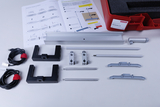 Das Bild zeigt eine Zusammenstellung von Teilen für ein Experimentiergerät, darunter Aluminiumprofile, Halterungen und Kabel. Zusätzlich gibt es eine Anleitung, die die Nutzung und den Zusammenbau der Komponenten beschreibt.