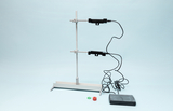 Das Bild zeigt eine Experimentierstation mit einer Halterung, die zwei Messgeräte und ein Display umfasst. Daneben befinden sich zwei farbige Ringe, die wahrscheinlich zur Durchführung von Experimenten oder Messungen verwendet werden.