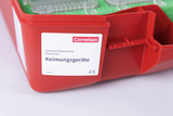 Das Bild zeigt eine rote Box mit dem Etikett "Keimungsgeräte" aus dem Cornelsen Experimenta Klassensatz. In der Box befinden sich verschiedene Geräte, die wahrscheinlich für Experimente zur Keimung von Pflanzen verwendet werden.