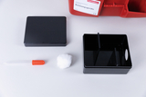 Das Bild zeigt ein Set für Experimentierbedarf mit einem roten Behälter und verschiedenen Zubehörteilen. Zu den enthaltenen Objekten gehören eine schwarze Box mit einem Deckel, eine Pipette mit rotem Griff und ein Stück Watte.