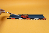 Das Bild zeigt eine wissenschaftliche Experimentieranordnung, bestehend aus einer mit zwei Motoren ausgestatteten kleinen Plattform auf einer Schiene. In der Hand hält jemand ein Messgerät, das wahrscheinlich für den Experimentierprozess verwendet wird.