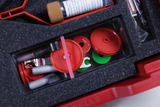 Das Bild zeigt eine rote Kunststoffbox, die mit verschiedenen Experimentiermaterialien gefüllt ist. Darunter befinden sich farbige Kreise, Röhrchen und weitere Utensilien, die alle in einer schützenden Schaumstoffeinlage angeordnet sind.