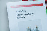 Das Bild zeigt einen Teil eines Katalogs für Experimentierbedarf, der sich auf die Themen Elementarphysik und Elektrik konzentriert. In der Mini-Box sind verschiedene Komponenten abgebildet, die für physikalische Experimente verwendet werden können.