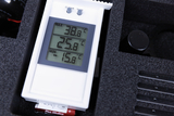 Das Bild zeigt ein digitales Thermometer, das aktuelle, maximale und minimale Temperaturen anzeigt. Es ist in einem stabilen Gehäuse platziert, das offenbar für den Einsatz im Bildungsbereich gedacht ist.