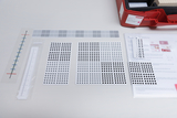 Das Bild zeigt verschiedene Platten mit Punkten in unterschiedlichen Farbtönen, die vermutlich für mathematische Experimente verwendet werden. Zudem sind ein Messlineal und eine Anleitung sichtbar, die auf den edukativen Zweck hinweisen.