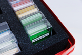 Das Bild zeigt ein Set von transparenten Karten in einem roten Koffer, die in Schaumstoff eingelegt sind, um sie zu schützen. Auf einer der Karten ist der Text "Kartensatz D1A 2.1" zu erkennen, was auf ein Experimentier- oder Lernmaterial hindeutet.