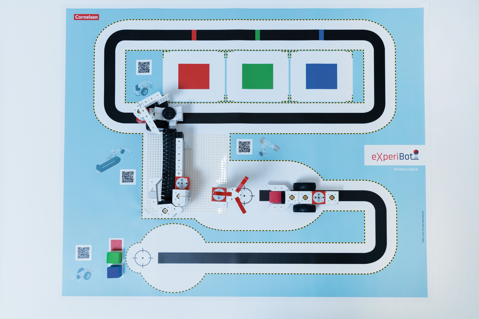 Das Bild zeigt eine Experimentierplattform mit einem drehbaren Roboter und einer farbigen Strecke zum Programmieren und Testen. Neben der Strecke befinden sich verschiedene QR-Codes und farbige Elemente, die für interaktive Lernaktivitäten verwendet werde