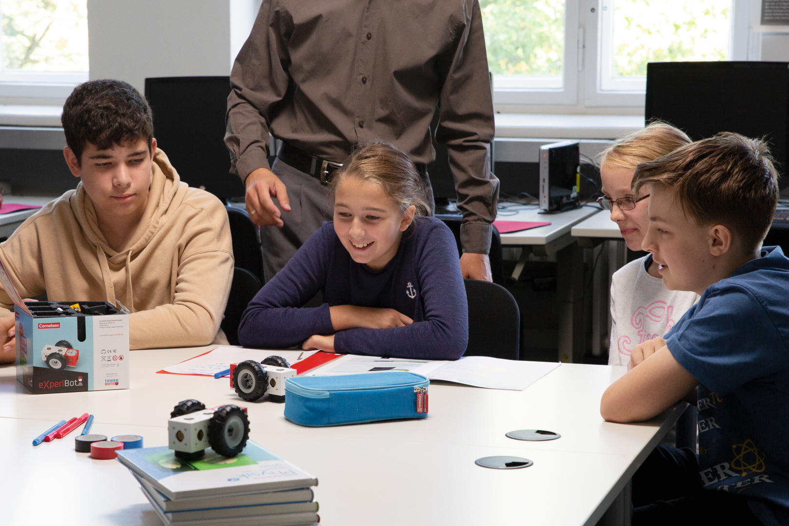 Das Bild zeigt eine Gruppe von Schülern, die begeistert an einem Tisch sitzen und sich mit einem Experimentierroboter beschäftigen. Sie sind umgeben von Schulmaterialien und einer ansprechenden Lernumgebung, die Kreativität und Teamarbeit fördert.