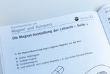 Das Bild zeigt eine Seite aus einem Lehrbuch über Experimente mit Magneten und Kompassen. Es beschreibt die Inhalte einer Magnet-Ausstellung für Lehrer, einschließlich einer Liste verschiedener Magnettypen, die im Experiment verwendet werden können.