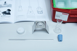 Das Bild zeigt ein Experimentier-Set mit verschiedenen Materialien, darunter ein Becherglas, eine Metallhalterung, eine Kerze und ein Glasröhrchen. Außerdem ist ein Lehrbuch mit Anleitungen für Experimente zum Thema Wärme zu sehen.
