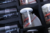 Das Bild zeigt eine Anordnung von Experimentiergeräten, darunter mehrere transparente Zylinder und mechanische Komponenten in einem gepolsterten Kasten. Die Teile scheinen für experimentelle Zwecke im Bildungsbereich konzipiert zu sein und sind sicher ver