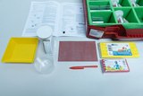 Das Bild zeigt ein Set für Experimentierzwecke im Bildungswesen, bestehend aus verschiedenen Materialien und Utensilien. Dazu gehören ein Messbecher, eine Waage, Bastelmaterialien sowie Anleitungen zum Thema "Schwimmen und Sinken".