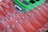 Das Bild zeigt eine Anordnung von transparenten Reagenzgläsern auf einer rotem Halterung, die für Experimentierzwecke im Bildungsbereich genutzt werden. Im oberen Bereich sind zudem weitere Materialien und Zubehörteile in einem grünen Einsatz sichtbar.