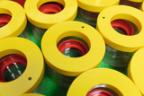 Das Bild zeigt eine Ansammlung von transparenten Behältern mit gelben Deckeln und roten Einsätzen. Die Behälter sind symmetrisch angeordnet und stehen auf einer grünen Unterlage, die einen frischen, plastischen Eindruck vermittelt.