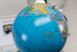Das Bild zeigt einen bunten Globus, der die politischen Grenzen und Geografie verschiedener Länder übersichtlich darstellt. Im Hintergrund ist ein Informationsblatt zu sehen, das anscheinend zusätzliche Erläuterungen oder Produkte anbietet.