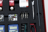 Das Bild zeigt ein Set für experimentelle Elektronik mit verschiedenen Komponenten wie Widerständen, Lampen, Krokodilclips, Messgeräten und Batterien, alles ordentlich in einem Schaumstoff-Einsatz angeordnet. Die Materialien sind ideal für den Einsatz im 