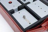 Das Bild zeigt eine rote Aufbewahrungsbox, die mehrere graue Experimentiervarianten in schützenden Schaumeinlagen enthält. Einer der angezeigten Schaltkreise weist eine Feder und eine Metallplatte auf, was auf experimentelle Anwendungen hindeutet.