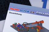 Das Bild zeigt die Bauanleitung für ein fischertechnik Experimentierset. Auf dem Cover sind farbige Illustrationen einesModells zu sehen, das mit verschiedenen mechanischen Komponenten aufgebaut werden kann.
