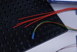 Das Bild zeigt ein schwarzes Steckbrett mit mehreren roten Drähten und einem farbigen Kabel, das aus mehreren Adern besteht. Außerdem ist eine blaue Verbindung sichtbar, die für Experimente im Bildungsbereich verwendet werden kann.