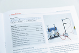 Das Bild zeigt eine Seite aus einem Katalog für Experimentierbedarf, auf der das Experiment "Zündkerze" beschrieben wird. Zu sehen sind technische Daten und Materialien, sowie eine Abbildung des zugehörigen Versuchsaufbaus mit anschlussfähigen Komponenten.