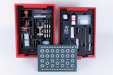 Das Bild zeigt eine rot gehaltene Aufbewahrungsbox, die mit verschiedenen Experimentiermaterialien ausgestattet ist, darunter elektrische Komponenten, chemische Substanzen und Werkzeug. In der Mitte des Sets befindet sich eine Leiterplatte mit mehreren Kontakten, die für Experimente genutzt werden kann.