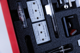 Das Bild zeigt eine Auswahl an Experimentiermaterialien in einer gepolsterten Box, darunter Messgeräte mit verschiedenen Spannungsangaben. Zu erkennen sind mehrere Stecker und einsichtbare Skalen, die für schulische Experimente genutzt werden können.