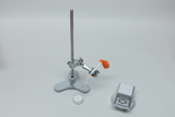 Das Bild zeigt ein Experimentiersetup, das aus einem stabilen Halter, einer Klemme für ein Reagenzglas und einer digitalen Waage besteht. Neben dem Setup liegt eine kleine Kerze, die vermutlich zur Durchführung eines Experiments verwendet wird.