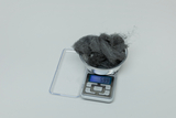 Auf dem Bild ist eine elektronische Waage zu sehen, auf der eine Schale mit grauem, fusseligem Material platziert ist. Die Anzeige der Waage zeigt ein Gewicht von 5,99 Gramm an.