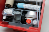 Das Bild zeigt einen roten Experimentierkasten, der verschiedene Materialien und Werkzeuge enthält, darunter Flaschen, ein Röhrchen, und einen Refillschreiber. Der Inhalt ist für den Einsatz in Bildungseinrichtungen konzipiert und unterstützt praktische Experimente.