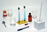 Das Bild zeigt verschiedene Labormaterialien, darunter Reagenzgläser mit blauer Flüssigkeit, Bechergläser und Chemikalien in Flaschen. Dazu sind Utensilien wie ein Löffel und ein Pipetten aus Kunststoff zu sehen, die für Experimente genutzt werden können.