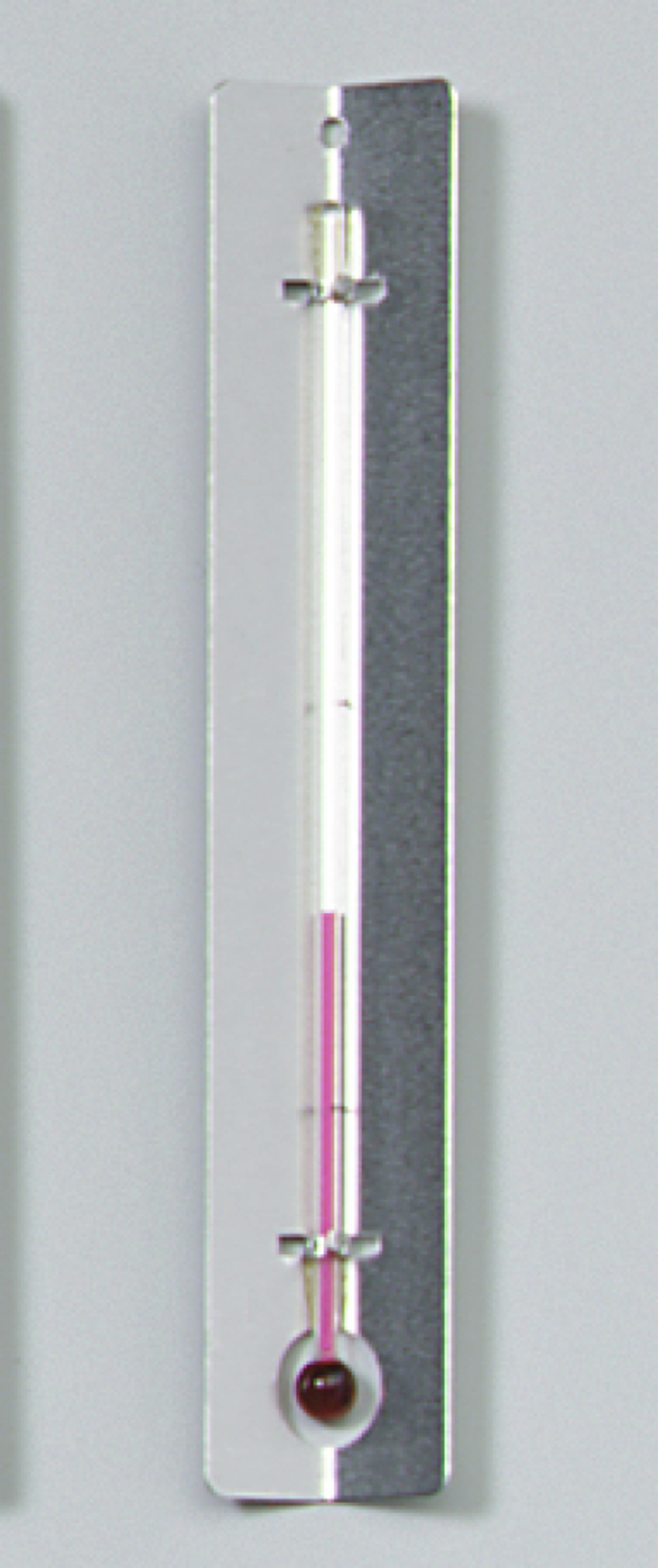 Das Bild zeigt ein Thermometer mit einer farbigen Skala und einer runden Quecksilberkugel am Ende. Es ist auf einer schlichten, hellen Hintergrundplatte befestigt, die es als Experimentiergerät für den Bildungsbereich kennzeichnet.