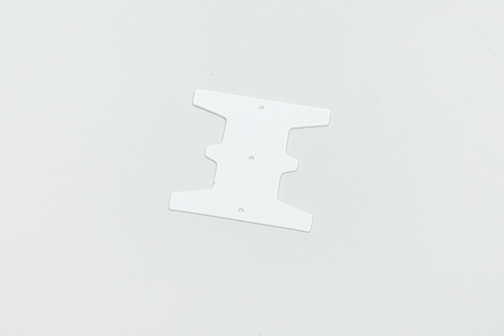 Das Bild zeigt eine weiße, flache Kunststoffschablone mit einer speziellen Form, die mehrere Aussparungen aufweist. Sie scheint für experimentelle oder kreative Aktivitäten im Bildungswesen konzipiert zu sein, möglicherweise als Teil eines Bausatzes oder zur Herstellung von Modellen.