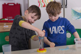 Auf dem Bild sind zwei Kinder zu sehen, die mit einem Experimentiergerät arbeiten, das Wasser enthält. Die Jungen sind sichtbar begeistert, während sie gemeinsam an dem Experiment arbeiten und dabei Spaß haben.