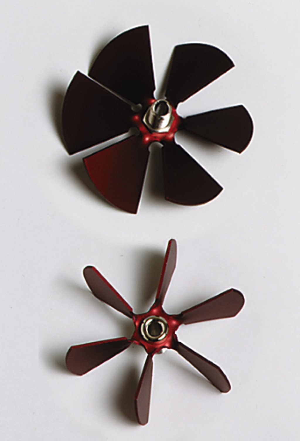 Das Bild zeigt zwei Modellpropeller in verschiedenen Größen, die aus einem metallischen Material gefertigt sind und eine rot-schwarze Farbgebung haben. Diese Propeller könnten für Experimente im Bereich der Fluiddynamik oder Aerodynamik im Bildungswesen verwendet werden.