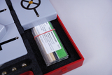 Das Bild zeigt eine Experimentierbox mit verschiedenen Materialproben und technischen Komponenten, die zur Durchführung von Experimenten im Bildungsbereich dienen. Unter den Proben befinden sich Materialien wie Aluminium, Glas und Holz, die zur Analyse genutzt werden können.