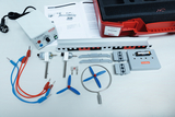 Das Bild zeigt ein Experimentierset zum Thema Windenergie, das verschiedene Komponenten wie Motoren, Kabel und Propeller umfasst. Zudem sind eine Anleitung und eine rote Aufbewahrungsbox zu sehen, die die Materialien organisiert.