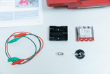 Das Bild zeigt Experimentiermaterialien, darunter eine Batteriefassung, eine Batteriepackung, eine Glühlampe, Anschlusskabel mit Krokodilklemmen und eine Lampenfassung. Diese Komponenten eignen sich für Lehr- und Lernzwecke im Bereich Elektrotechnik.
