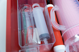 Das Bild zeigt eine transparente Box mit verschiedenen Experimentierutensilien, darunter Glaskolben, Spritzen und Messbehälter. Alles ist ordentlich angeordnet und bereit für den Einsatz im Bildungsbereich.