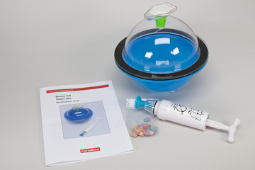 Das Bild zeigt ein Demo-Set namens "Virus-Ufo" samt Anleitung und Zubehör. Im Set enthalten sind ein blauer Behälter, eine Spritze mit einem fröhlichen Gesicht und eine Tüte mit bunten, kleinen Teilchen.
