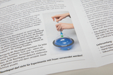 Das Bild zeigt eine Person, die eine Hand-Vakuumpumpe verwendet, um Luft aus einer transparenten Raumkapsel mit blauem Inhalt zu entfernen. Um die Kapsel herum sind Anweisungen zum sicheren Gebrauch und zur Reinigung abgedruckt.