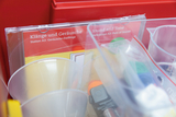 Das Bild zeigt einen Ausschnitt aus einem Experimentierkasten für das Bildungswesen, der Materialien zur Erkundung von Klängen und Geräuschen enthält. Auf der Verpackung sind die Titel „Klang und Geräusche“ sowie „Sound and Tone“ zu sehen, zusammen mit transparenten Behältern und Utensilien.