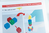 Das Bild zeigt eine Anleitung zum Experimentieren mit Hebel, Rolle und Magnet. Zwei Abbildungen illustrieren, wie verschiedene farbige Würfel gestapelt werden können, während die Hand einer Person eine gelbe Figur aufnimmt.