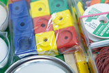 Das Bild zeigt eine Vielzahl von Experimentiermaterialien, darunter bunte Würfel und Rollen, die in einer transparenten Verpackung untergebracht sind. Ergänzt wird das Set durch verschiedene runde Objekte und Gummibänder, die für praktische Lernaktivitäten geeignet sind.