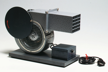 Das Bild zeigt ein Experimentiergerät in Form eines Ventilators mit einem runden Deckel und einem rechteckigen Auslass. Das Gerät wird mit einem Stromkabel betrieben und eignet sich für Bildungszwecke im Bereich Physik oder Technik.